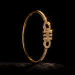 A gold hinged bangle bracelet with a central Chinese character design, embellished with pavé-set clear stones, photographed against a solid black background.