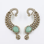 A pair of gold-toned crescent-shaped earrings with pavé-set clear stones and a central light green teardrop gemstone, shown on a plain white background.
