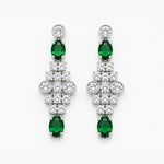 A pair of silver-tone drop earrings featuring oval-cut green emeralds and round-cut clear stones, arranged symmetrically on a light gray background.