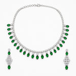 A silver-tone jewelry set featuring a collar necklace and matching drop earrings, both adorned with rows of clear stones and a series of oval-cut green emeralds hanging along the front, displayed on a clean white background.