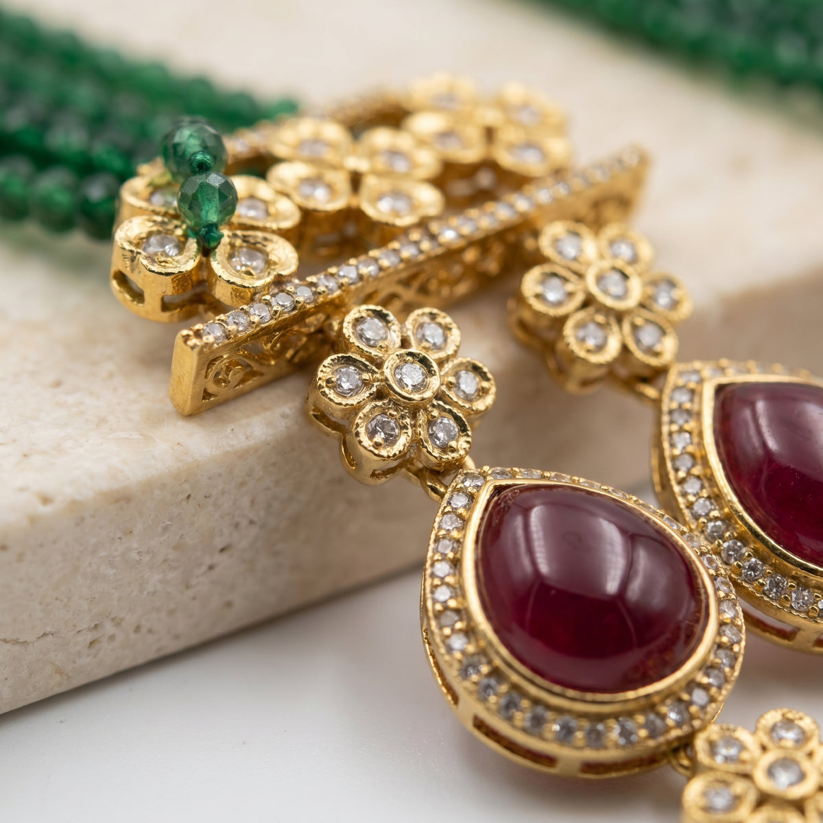 Gold-toned traditional Indian jewelry set featuring a decorative bar with floral motifs, a small green stone accent, and a teardrop-shaped drop with a deep red cabochon stone surrounded by clear crystals.