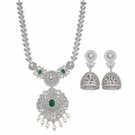 An ornate silver-toned jewelry set featuring a necklace and matching earrings. The necklace has a detailed filigree chain and a large pendant adorned with clear stones, a central green emerald-cut stone, and dangling white pearl beads.