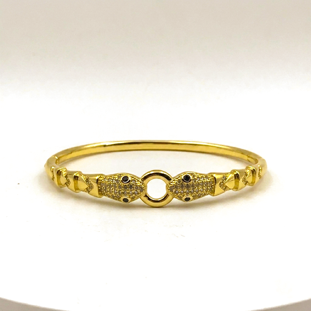 A gold-plated bangle bracelet with a central O-ring flanked by two fish-shaped motifs paved with small clear stones, set against a plain white background.