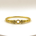 A gold-plated bangle bracelet with a central O-ring flanked by two fish-shaped motifs paved with small clear stones, set against a plain white background.