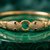 A gold bangle bracelet with two snake-head clasps paved with small clear stones and accented with black inlays, resting on a green marbled surface.