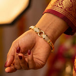 A close-up of a person's hand wearing a gold snake-link bracelet adorned with pavé-set clear stones and small black bead eyes, paired with a deep red and gold embroidered sleeve.