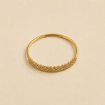 A gold huggie bangle bracelet featuring a textured, woven floral pattern along the front band, displayed on a warm beige background.