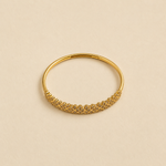A gold bangle bracelet with a textured, woven floral pattern along the front band, displayed on a warm beige background.