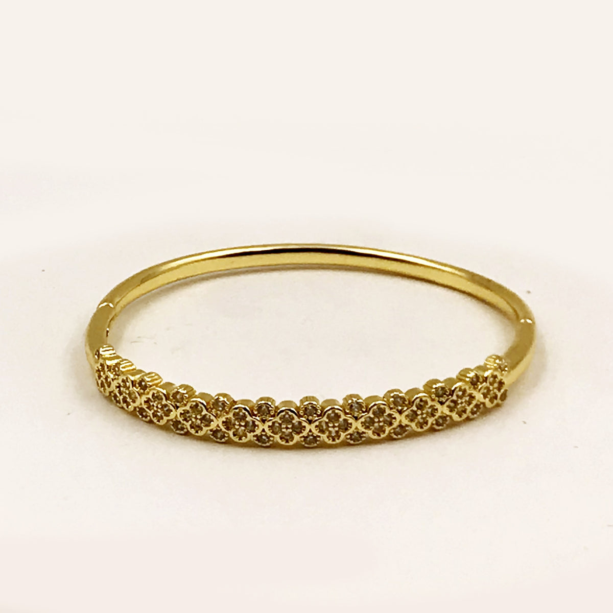 A gold bangle bracelet with a textured, floral-patterned front band, photographed on a plain white background.