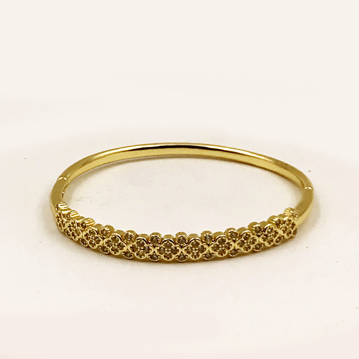 A gold bangle bracelet with a textured, floral-patterned front band, photographed on a plain white background.
