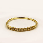 A gold bangle bracelet with a textured, floral-patterned front band, photographed on a plain white background.