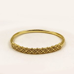 A gold bangle bracelet with a textured, floral-patterned front band, photographed on a plain white background.