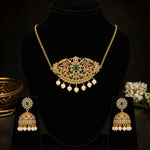 Gold-toned traditional jewelry set displayed on a black velvet mannequin bust, including a necklace with a floral pendant, matching earrings, and pearl drops. The jewelry features green and pink stone accents and gold metalwork.