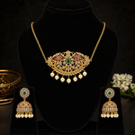Gold-toned traditional jewelry set displayed on a black velvet mannequin bust, including an ornate necklace with a central green teardrop stone, pink floral details, and dangling pearl-like beads, plus matching earrings on small black stands.