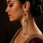 A woman in profile wearing a large traditional Indian jhumka earring with silver-toned metal, red enamel, and clear stones. The earring features a rectangular top with a red center, a silver border, and dangling chain elements with small red and silver accents.