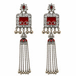 A pair of traditional Indian silver-toned earrings with red enamel panels, clear rhinestones, and dangling bell chains.