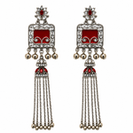 A pair of traditional Indian silver-toned tassel earrings with red enamel panels, clear rhinestones, and small hanging bells, shown on a plain white background.