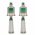 A pair of traditional Indian silver-toned dangle earrings with green enamel panels, clear pavé stones, and dangling gold-tone bells on a white background.