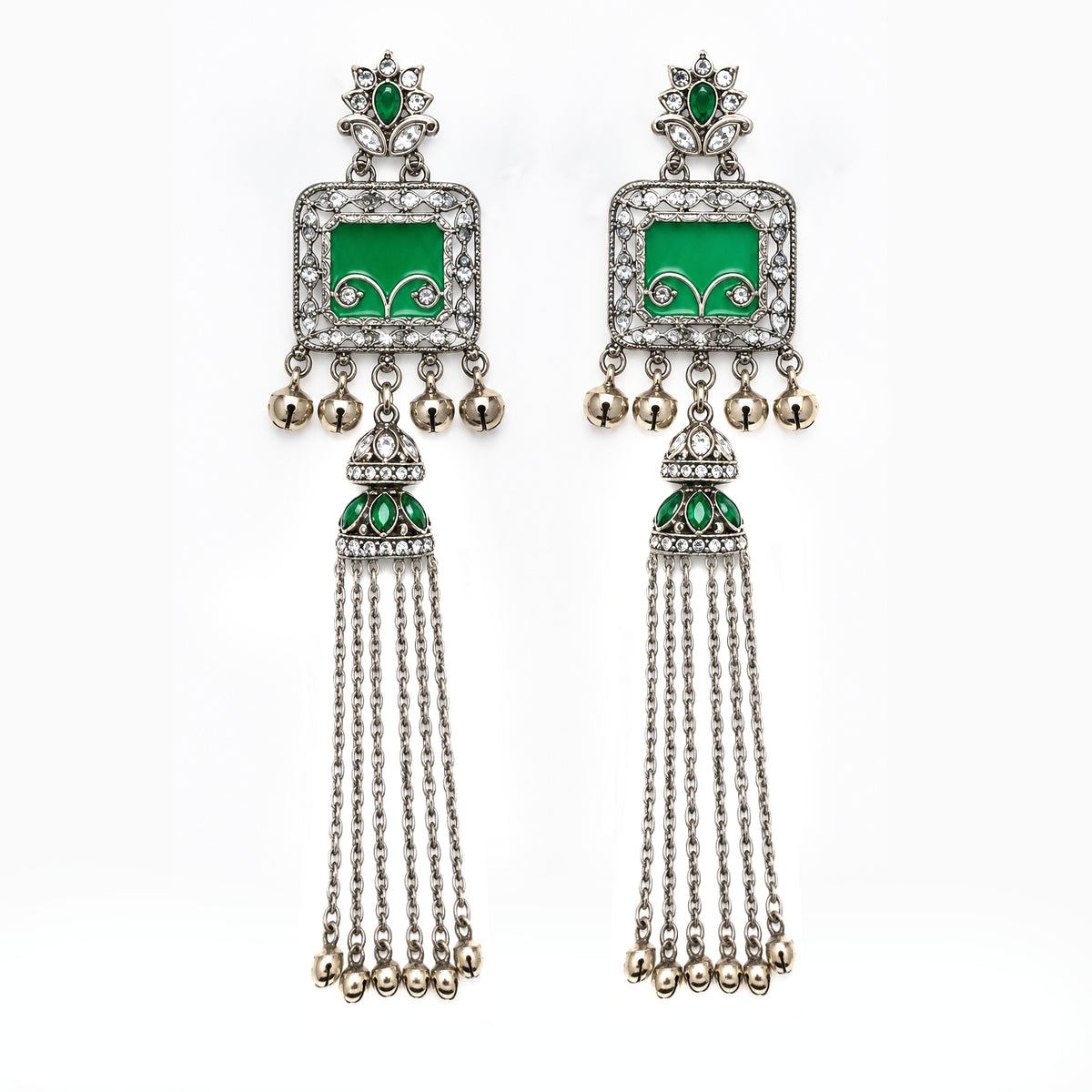 A pair of traditional Indian silver-toned dangle earrings with vibrant green enamel panels, clear pavé stones, and dangling silver chains ending in small gold-toned bells, shown against a plain white background.