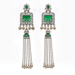 A pair of traditional Indian silver-toned dangle earrings with green enamel inlays, clear pavé stones, and dangling silver bells, shown against a plain white background.