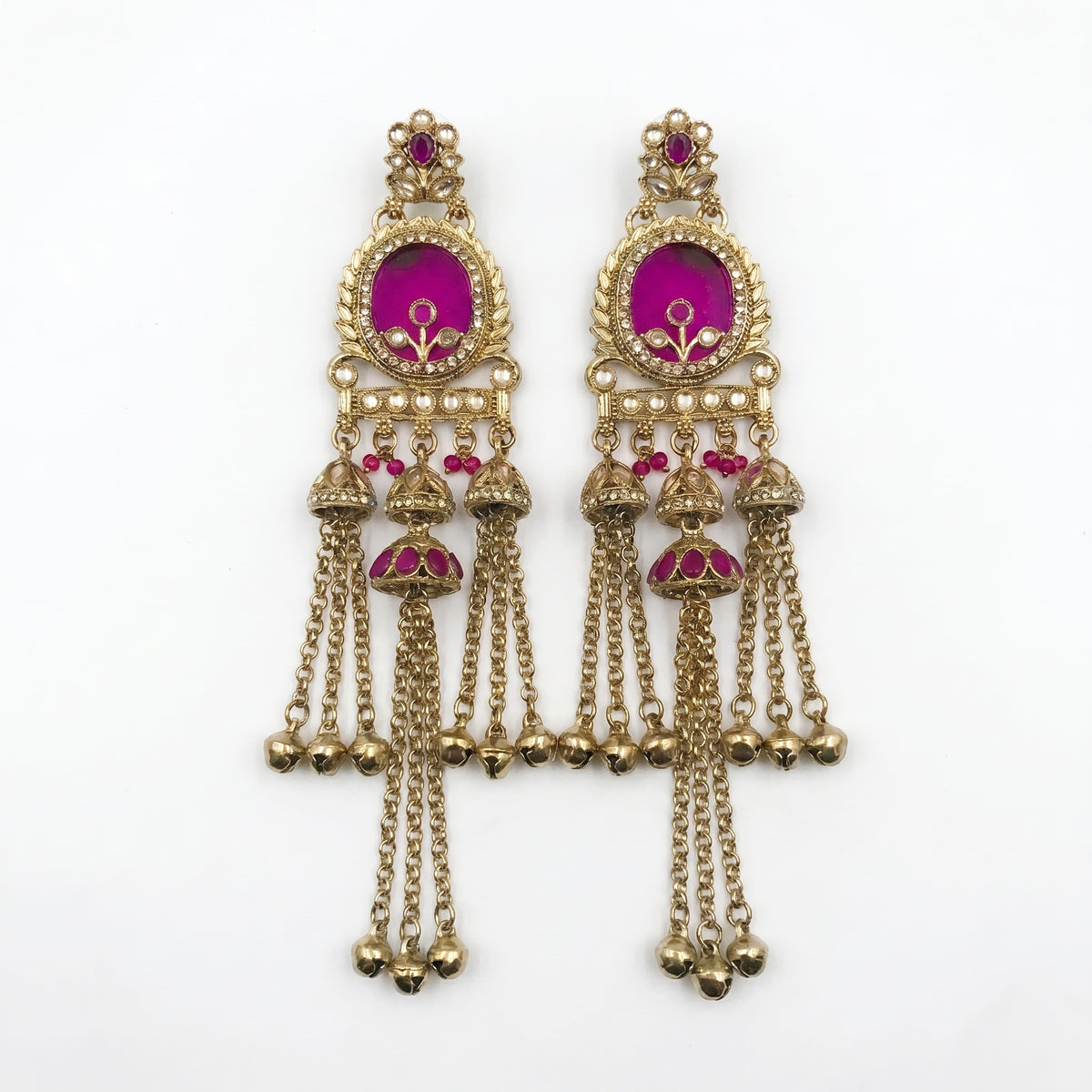 A pair of ornate gold-toned traditional Indian jhumka earrings with bright magenta-pink enamel inlays and dangling chain bells, shown on a plain white background.