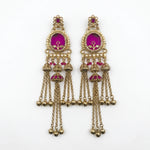A pair of ornate gold-toned traditional Indian jhumka earrings with bright magenta-pink enamel inlays and dangling chain bells, shown on a plain white background.