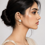 A woman in profile wearing a large gold-toned crescent-shaped ear cuff adorned with small pearls and a dangling pearl charm, shown against a light gray studio background.