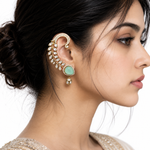 A close-up side profile of a woman wearing a large gold-toned ear cuff earring adorned with clear stones and a mint green oval stone, set against a clean white background.