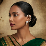 A woman in profile wearing a large, elegant gold-toned ear cuff adorned with clear stones, paired with a dark green saree against a textured gold background.