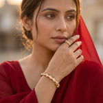 A woman in a red traditional outfit wearing a gold signet ring and a matching gold bracelet, captured in warm golden-hour lighting against a softly blurred background.