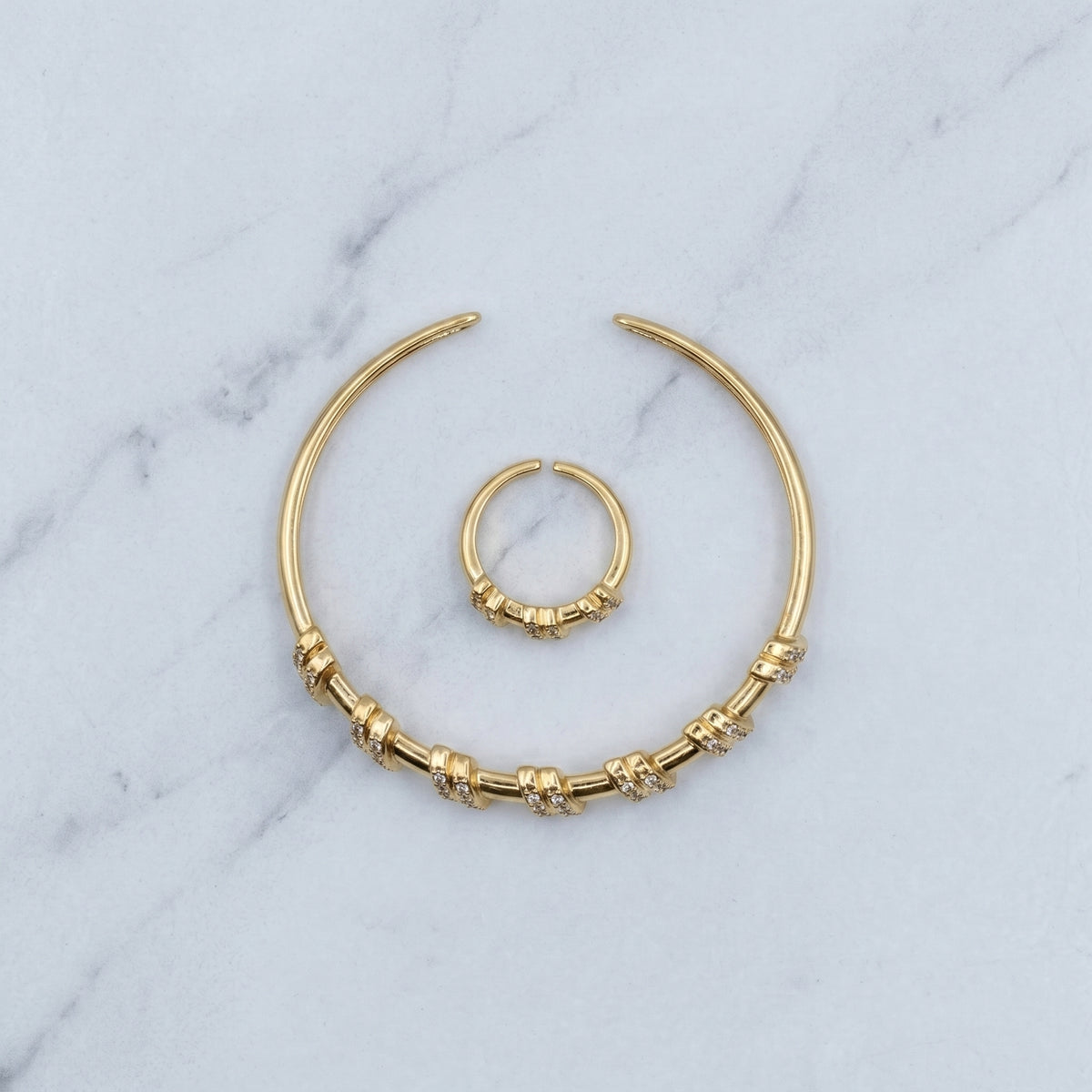 A pair of gold-toned body jewelry, including a large crescent-shaped ring with textured bead details and a smaller matching ring, displayed on a light gray marble surface.