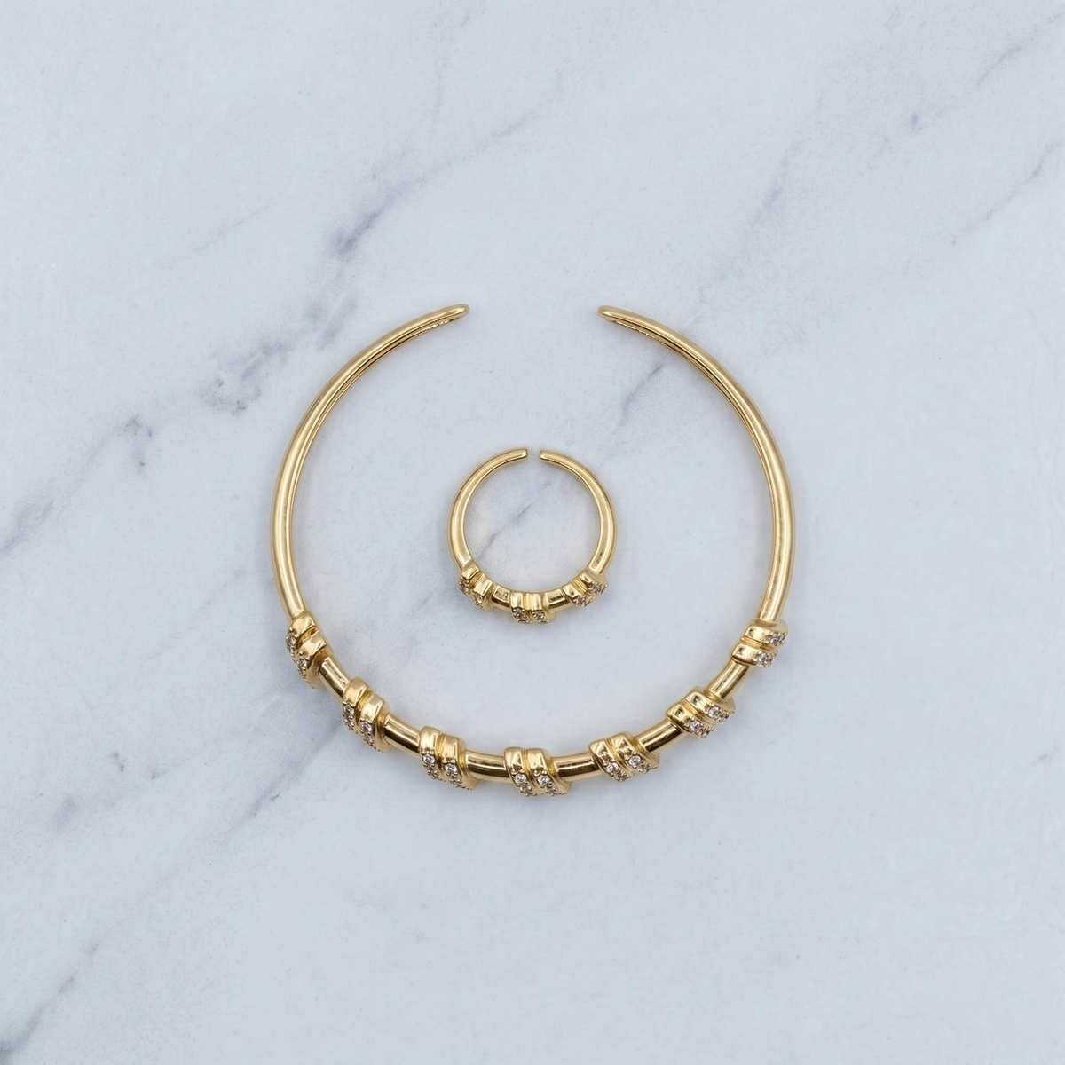 Gold-toned body jewelry set consisting of a large crescent hoop with textured bead details and a smaller matching curved ring, displayed on a white marble surface.