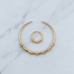 A pair of gold-toned body jewelry, including a large crescent-shaped ring with textured bead details and a smaller matching ring, displayed on a light gray marble surface.