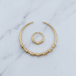 Gold-toned body jewelry set consisting of a large crescent hoop with textured bead details and a smaller matching curved ring, displayed on a white marble surface.