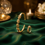 Gold-toned jewelry set featuring a cuff bracelet and matching ring, both adorned with rows of small clear stones, displayed on draped emerald green satin with a softly blurred luxury background.
