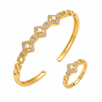 Gold-tone open cuff bracelet and matching ring set with diamond-shaped pavé settings and clear stones, shown on a plain white background.
