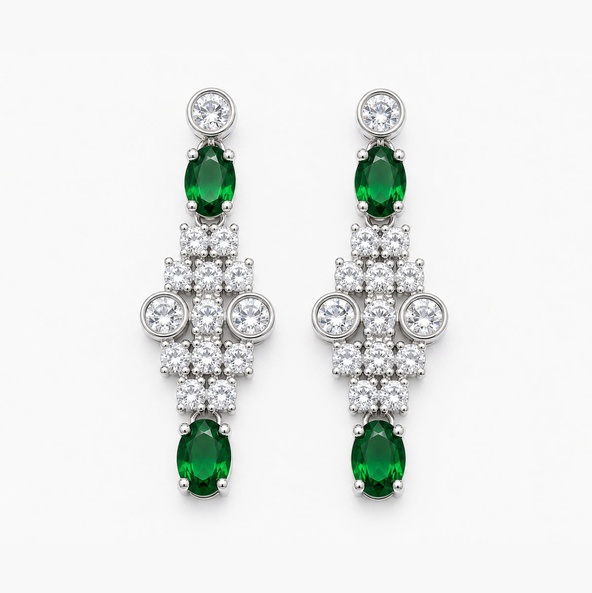 A pair of silver-tone drop earrings featuring oval-cut green emeralds and round-cut clear stones, arranged symmetrically on a light gray background.