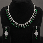A three-piece jewelry set featuring a silver-tone necklace and matching drop earrings with emerald-cut green gemstones and clear stones, displayed on a black velvet mannequin bust.