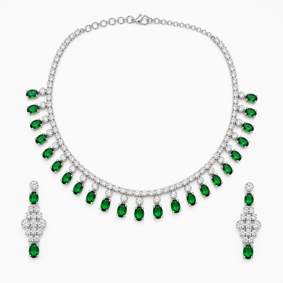 A silver-tone jewelry set featuring a collar necklace and matching drop earrings, both adorned with rows of clear stones and a series of oval-cut green emeralds hanging along the front, displayed on a clean white background.