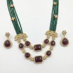 Gold and emerald green traditional Indian jewelry set featuring a multi-strand necklace with deep red gemstone accents and matching teardrop earrings.