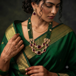 A woman wearing a rich green saree with gold zari borders and a large ornate gold statement necklace with deep red stones, styled with matching earrings.