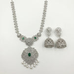 Silver-toned Indian jewelry set featuring a necklace and matching earrings, embellished with silver crystals, pearls, and small green emerald-cut stones, displayed on a clean white background.