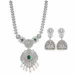 A silver-toned traditional Indian jewelry set featuring a necklace and matching earrings. The necklace has a detailed filigree chain and a large central pendant adorned with clear stones, a green rectangular emerald-cut stone, and small white pearl drops.
