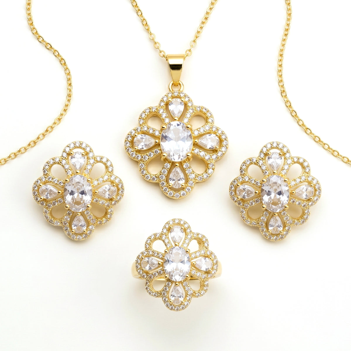 Gold jewelry set featuring a pendant necklace, ring, and two matching earrings, all with floral clover-shaped designs set with clear crystals on a white background.