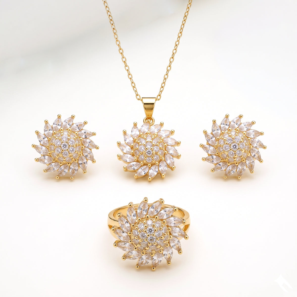 Gold-tone jewelry set featuring a pendant necklace, matching stud earrings, and a ring, each with a sunburst design set with clear marquise and round stones on a white background.