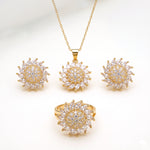 Gold-tone jewelry set featuring a pendant necklace, matching stud earrings, and a ring, each with a sunburst design set with clear marquise and round stones on a white background.